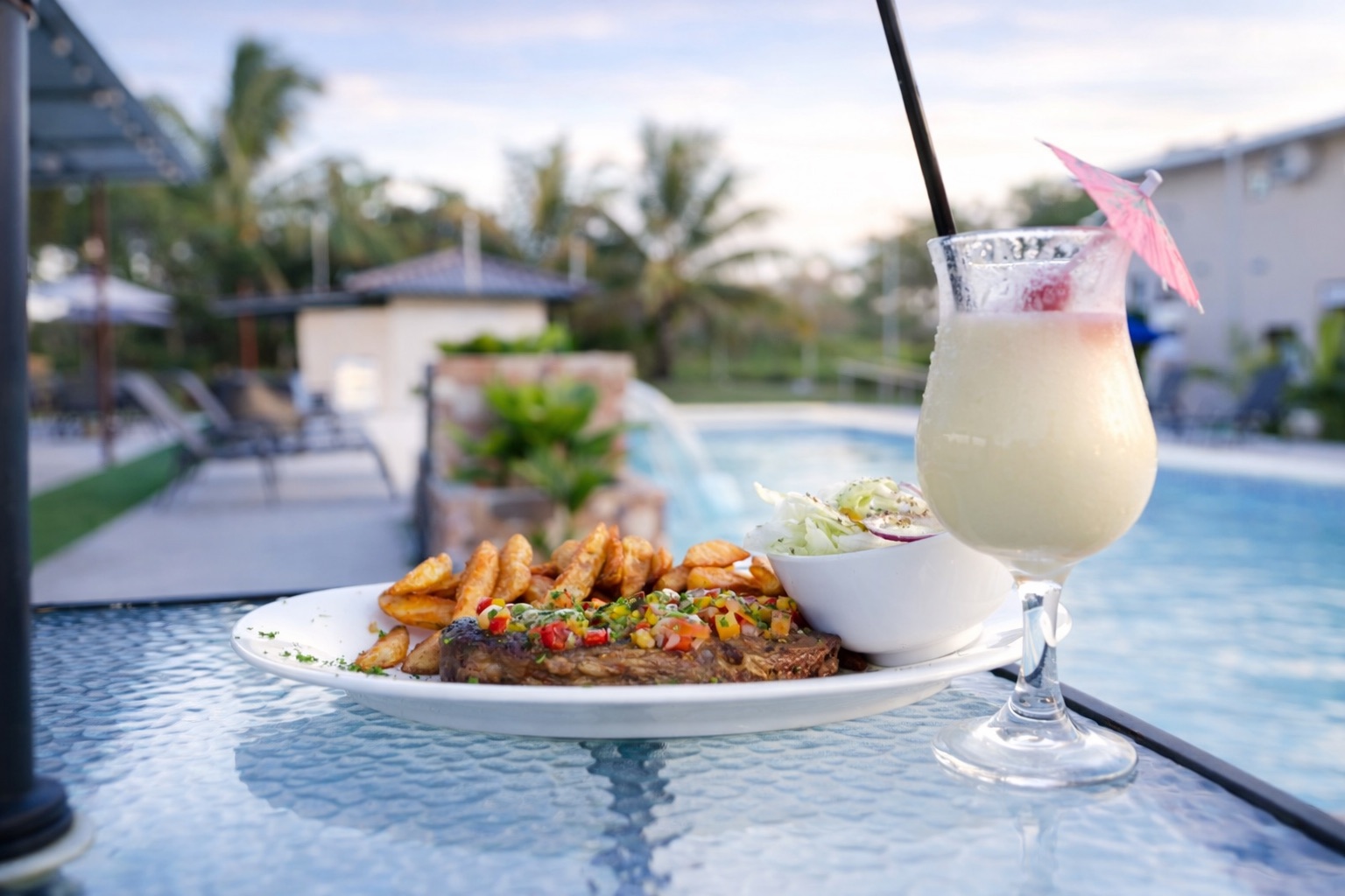 Plato de carne con papas y piña colada junto a la piscina del Hotel Mely